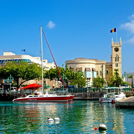 Circular aerial view of a tropical coastal town and harbor at sunset, featuring a large cruise ship, numerous sailboats, and lush green hills
